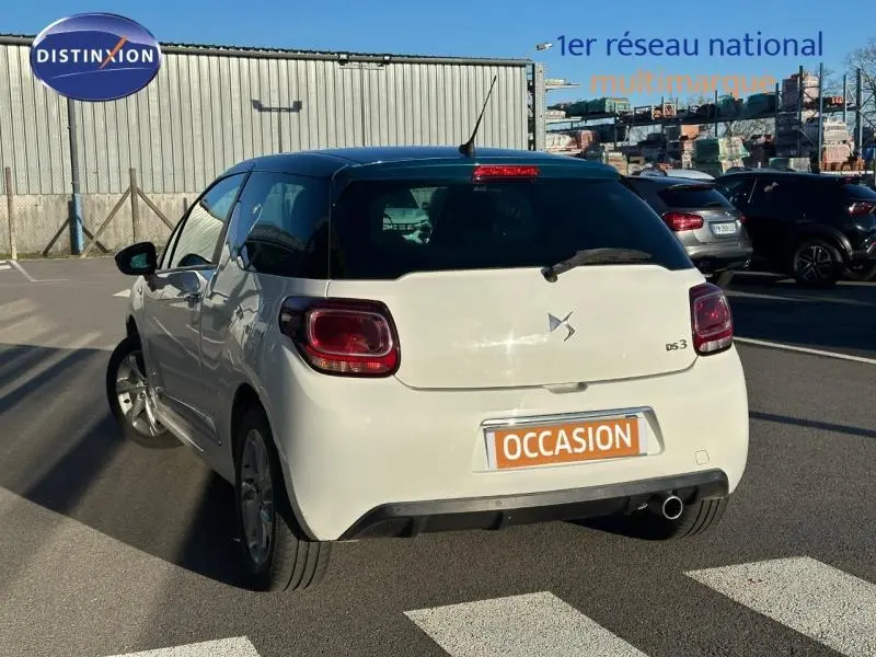 Vue 3/4 arrière droite d'une DS3 blanche avec toit noir et feux arrière LED, stationnée en extérieur sur parking.