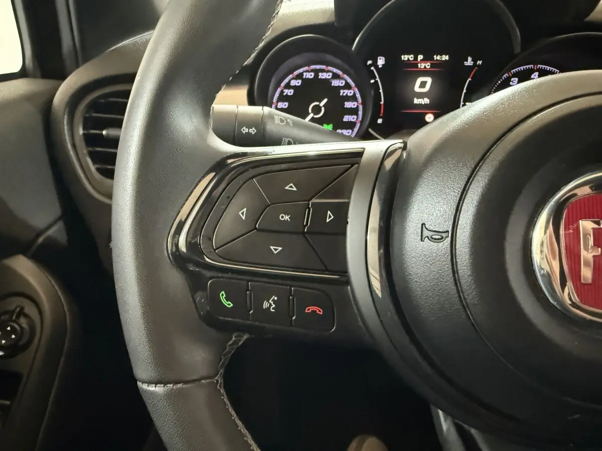 Gros plan sur le volant multifonctions noir de la Fiat 500X 2021 avec tableau de bord numérique en arrière-plan.