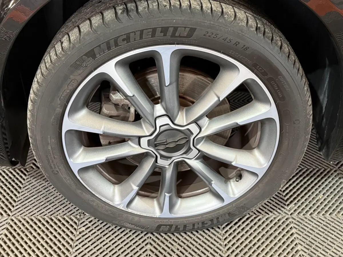 Gros plan sur la jante alliage argentée avec logo Fiat au centre, montée sur pneu Michelin du Fiat 500X noir.