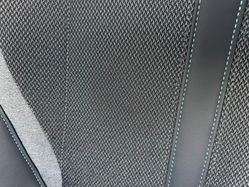 Gros plan sur le tissu noir et gris avec surpiqûres bleues du siège avant de la Peugeot 308 2024.