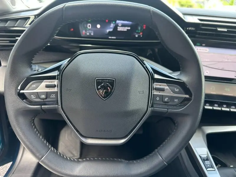 Vue rapprochée du volant multifonction noir de la Peugeot 308 2024 avec tableau de bord numérique en arrière-plan.