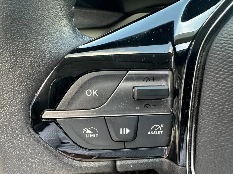 Gros plan sur les commandes du volant multifonction noir du Peugeot 308 2024, boutons de régulateur et limiteur de vitesse.