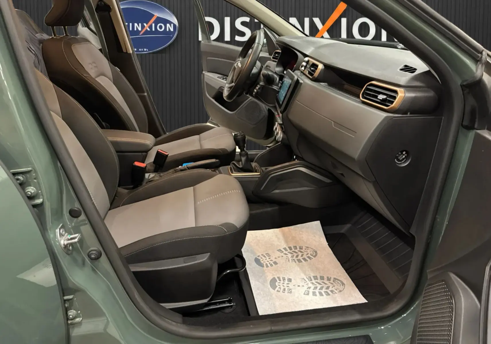 Vue intérieure côté conducteur du Dacia Duster 2024 kaki lichen, montrant sièges tissu gris et tableau de bord moderne.
