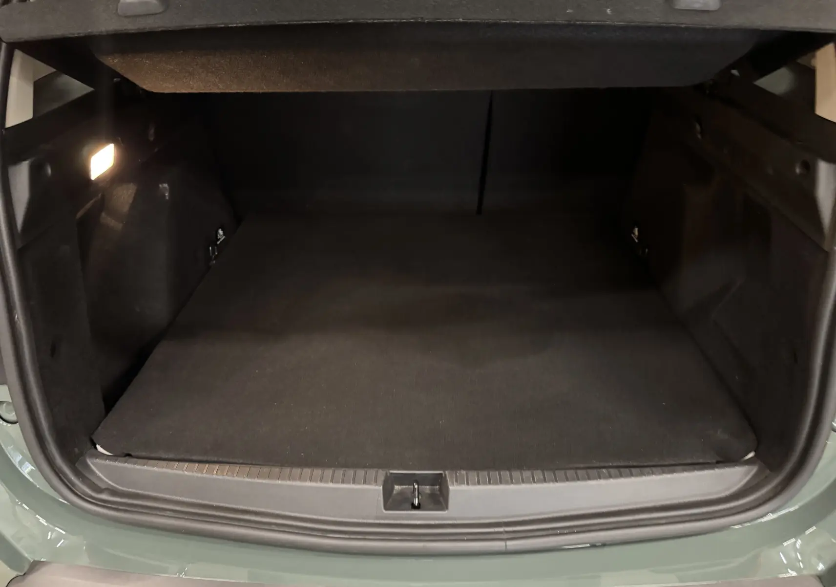 Coffre ouvert vu de l'arrière d'un Dacia Duster 2024 kaki lichen, espace de chargement vide et éclairé à gauche.