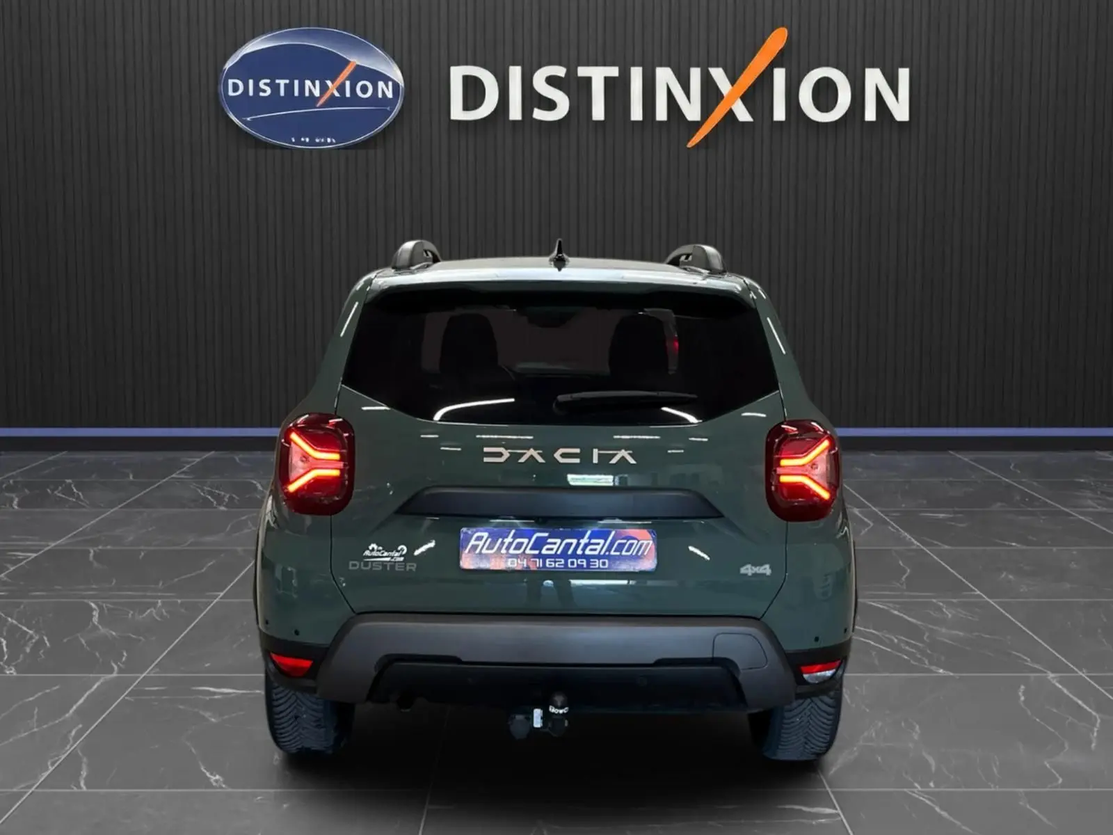 Vue arrière d'un Dacia Duster 2024 kaki lichen avec feux LED allumés et attelage visible en intérieur showroom.