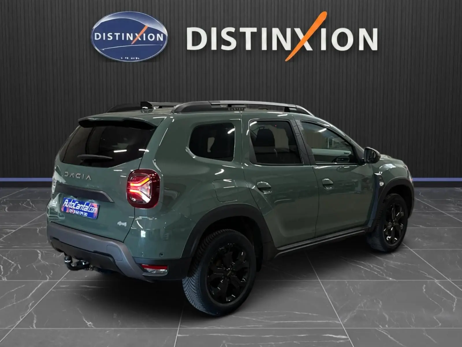 Vue 3/4 arrière droite du Dacia Duster 2024 kaki lichen avec jantes noires et attelage visible en intérieur showroom.