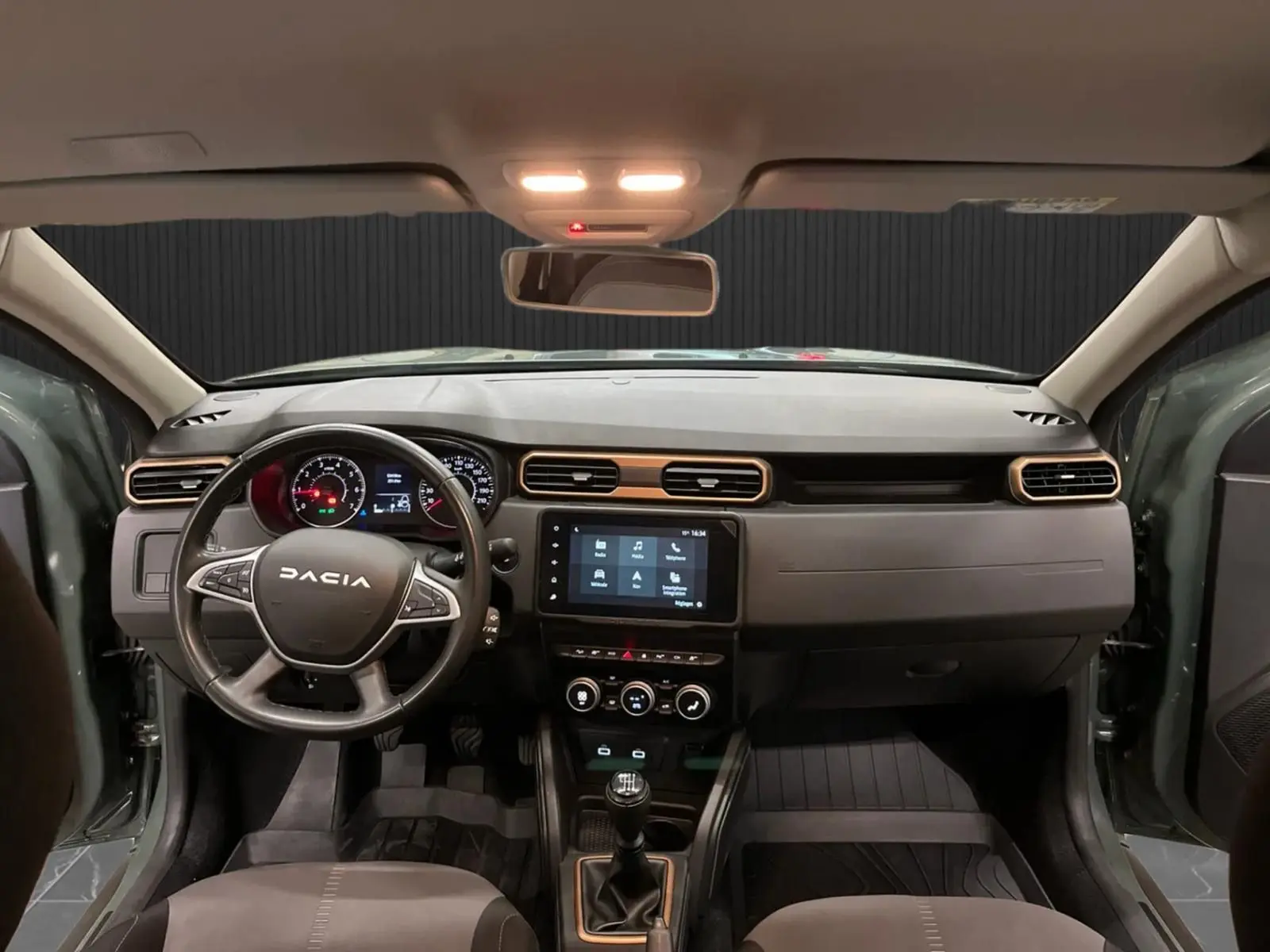 Vue intérieure frontale du Dacia Duster 2024 kaki lichen, mettant en valeur le tableau de bord et la console centrale avec écran tactile.