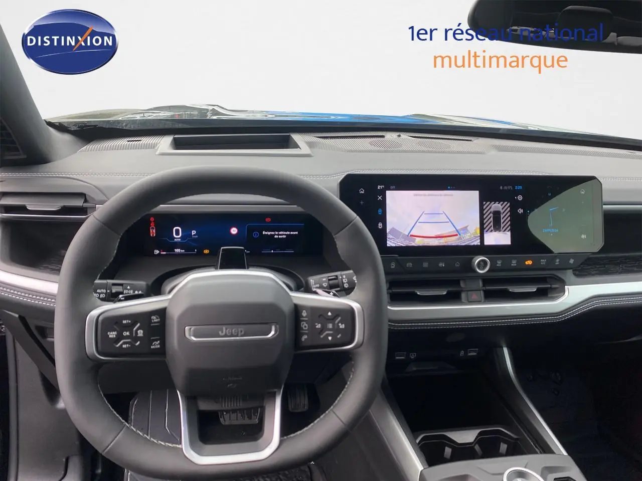 Vue intérieure centrée sur le volant Jeep noir avec tableau de bord numérique et écran tactile affichant la caméra de recul.