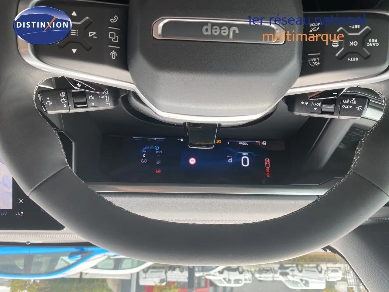Vue rapprochée du volant noir avec logo Jeep et commandes intégrées, tableau de bord digital en arrière-plan.