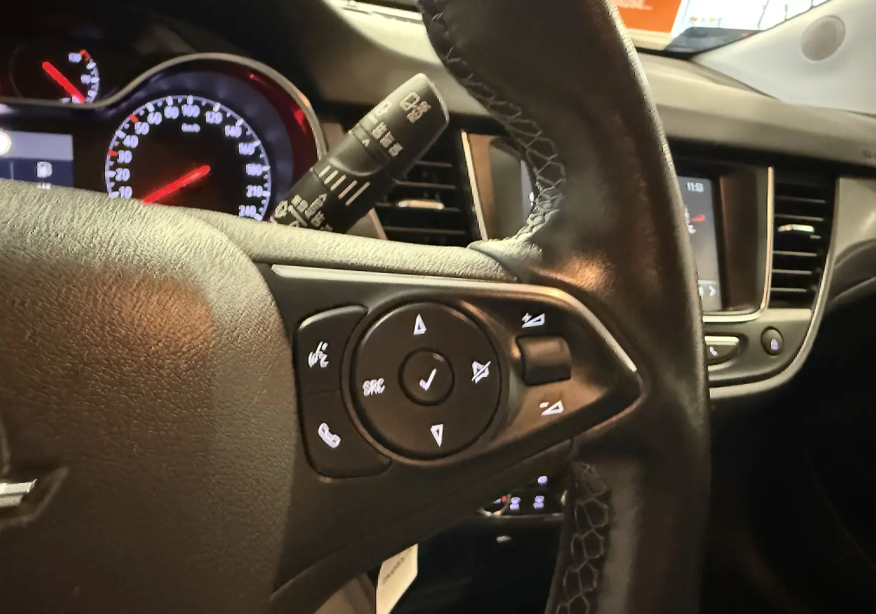 Gros plan sur le volant noir de l’Opel Crossland 2023, avec commandes intégrées et tableau de bord lumineux en arrière-plan.