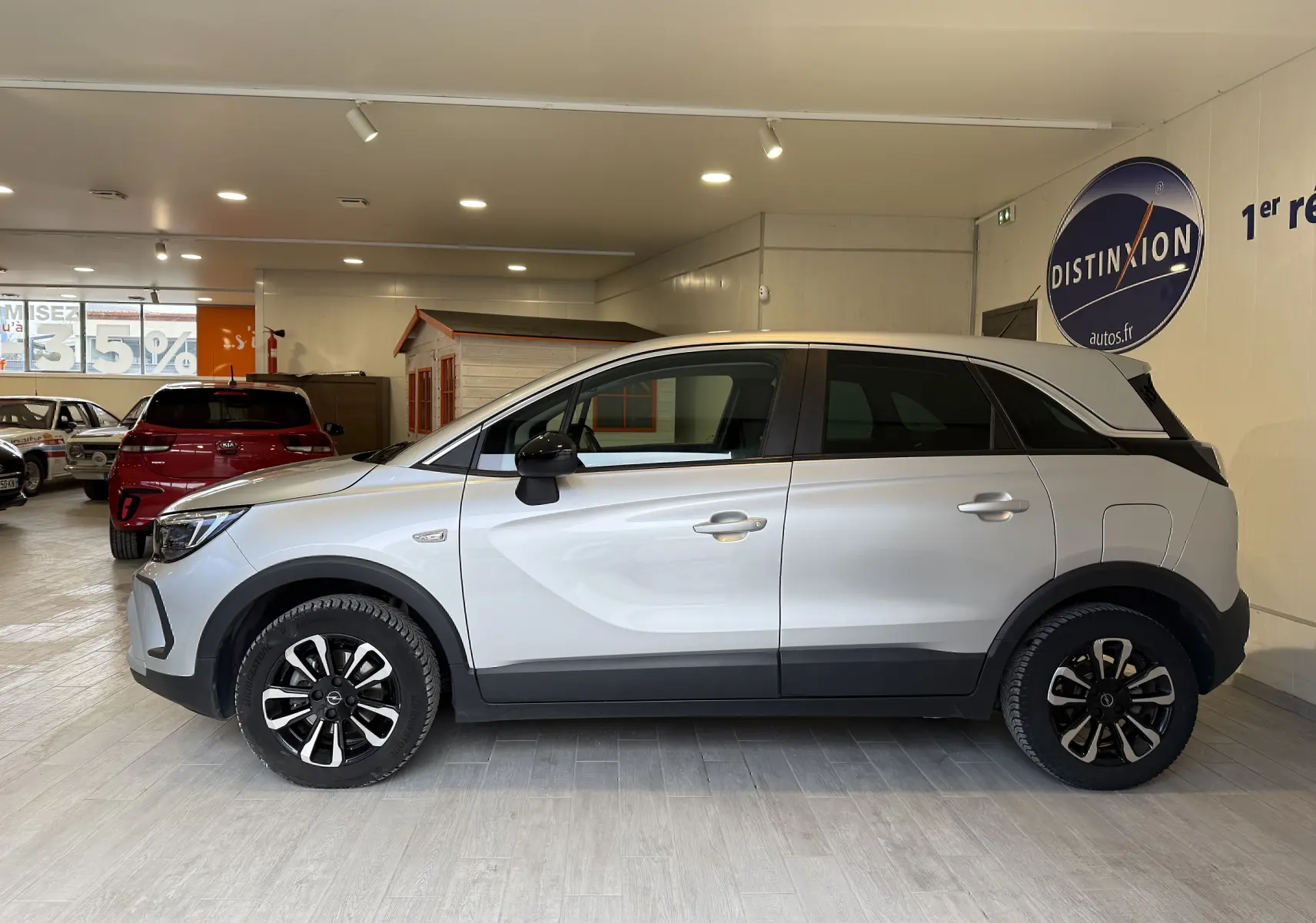 Vue de profil côté gauche d’un Opel Crossland gris 2023 avec jantes noires et toit contrasté en intérieur showroom.