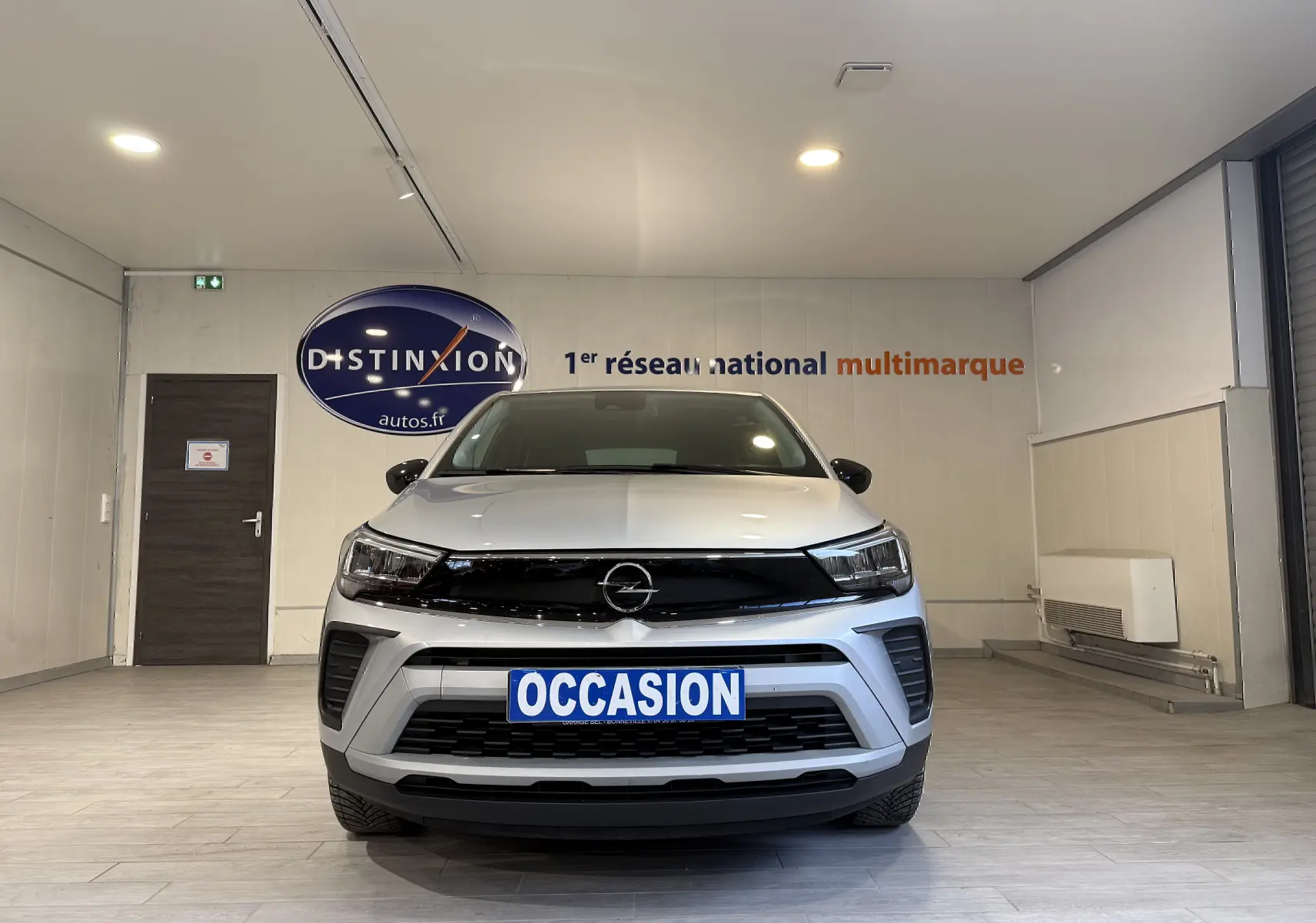 Vue frontale d’un Opel Crossland gris 2023 avec calandre noire et plaque « OCCASION » en intérieur showroom.