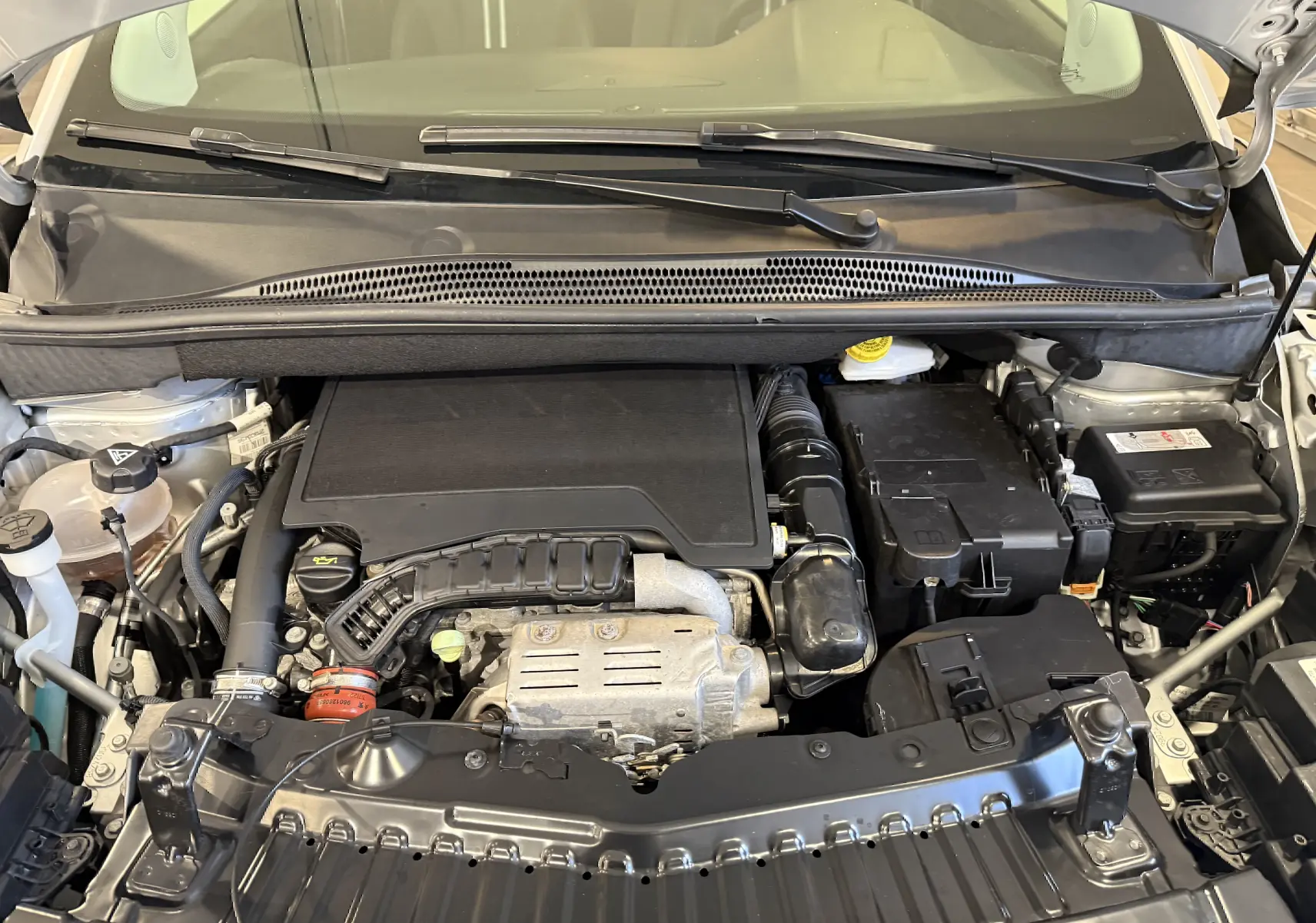 Vue rapprochée du moteur essence gris d'un Opel Crossland 2023, capot ouvert, montrant les composants sous le capot.