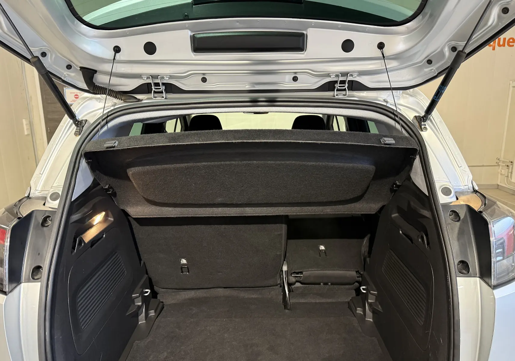 Vue arrière du coffre ouvert de l’Opel Crossland gris 2023, montrant la banquette arrière partiellement rabattue et le cache-bagages.