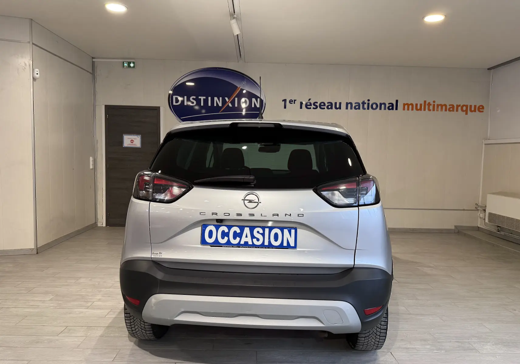 Vue arrière d'un Opel Crossland gris 2023 en intérieur, avec plaque "OCCASION" et feux arrière distinctifs.