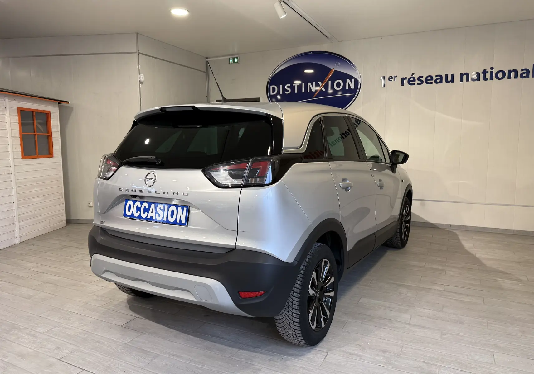 Vue 3/4 arrière droite de l’Opel Crossland gris 2023 avec feux LED et jantes alliage noires, en intérieur showroom.