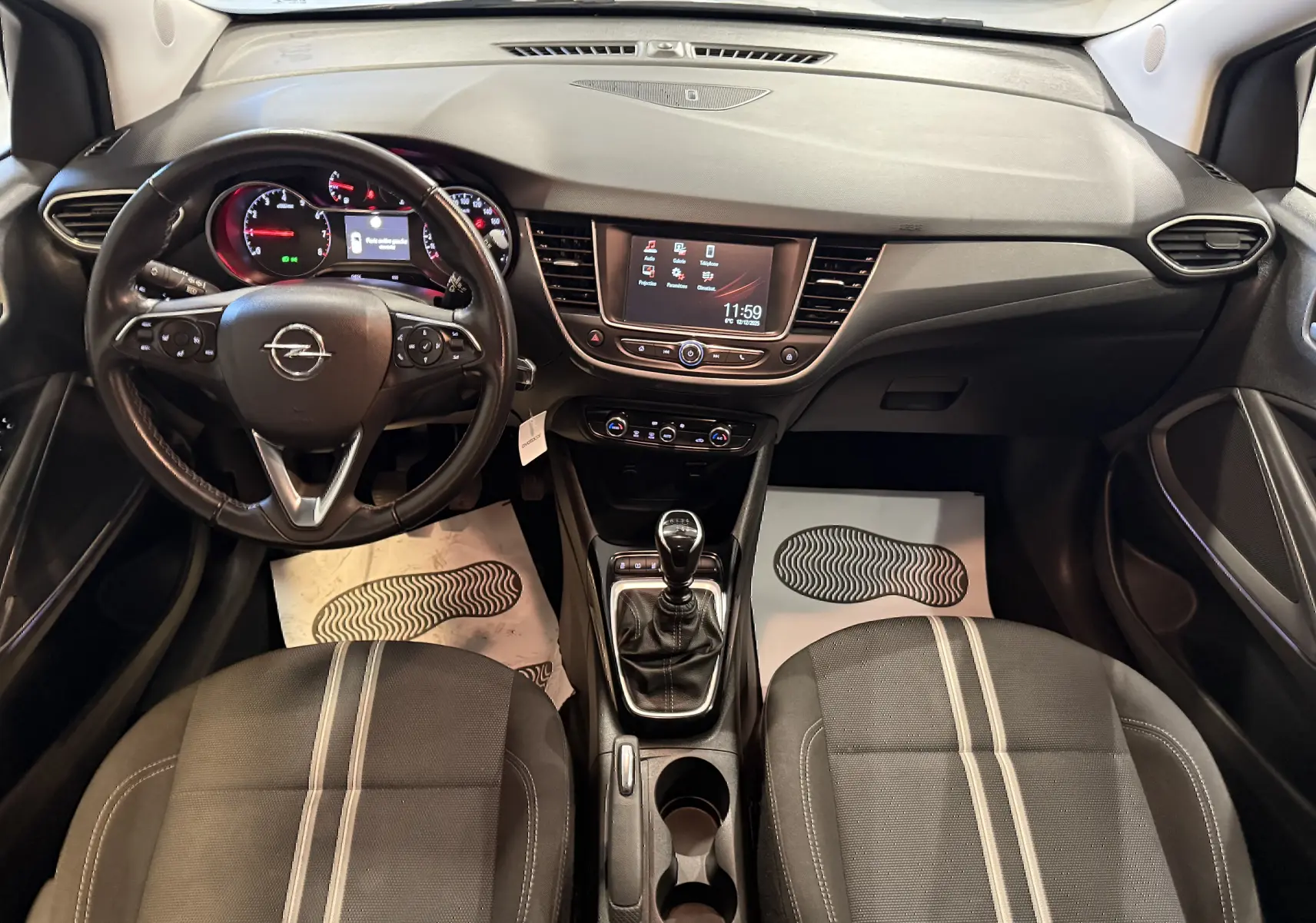 Vue intérieure avant de l’Opel Crossland gris 2023, avec tableau de bord moderne, volant multifonction et boîte manuelle.