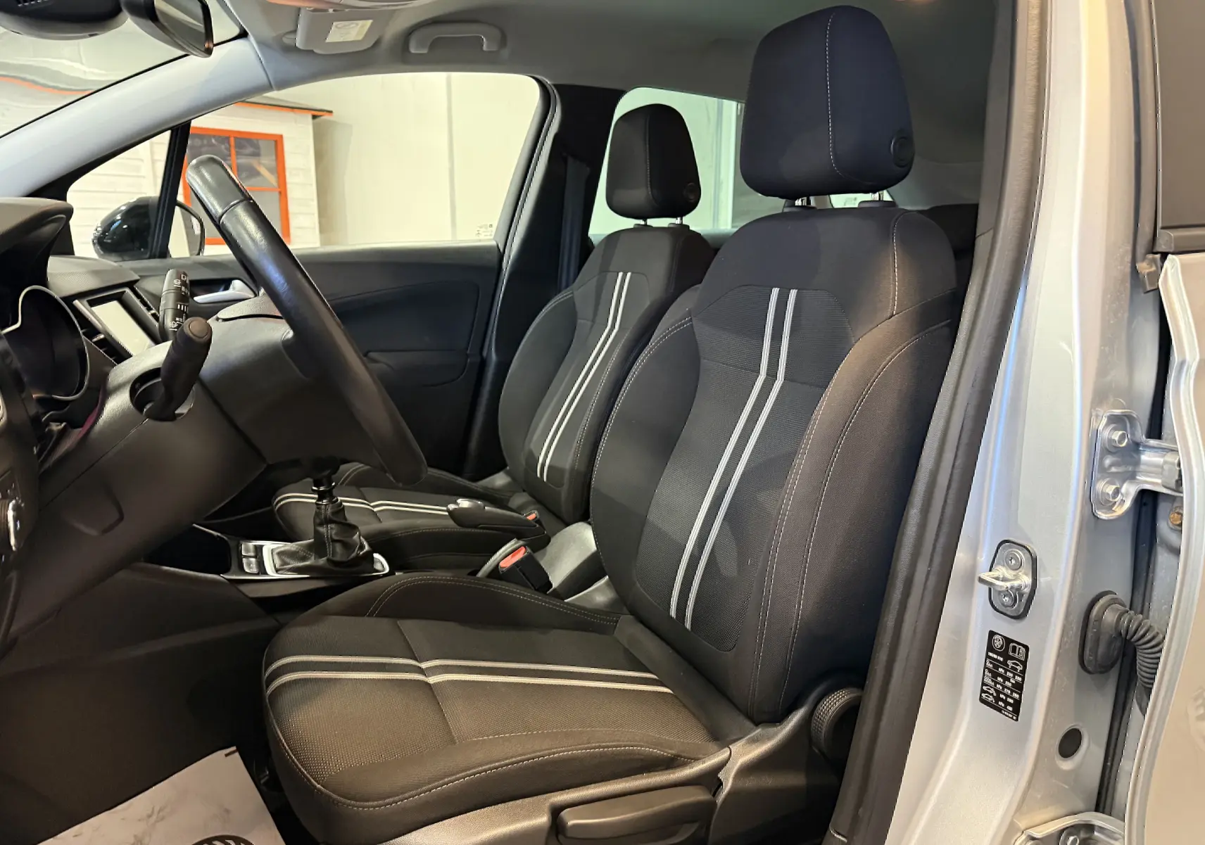Vue intérieure côté conducteur de l’Opel Crossland gris 2023, mettant en valeur les sièges noirs à bandes grises et la boîte manuelle.