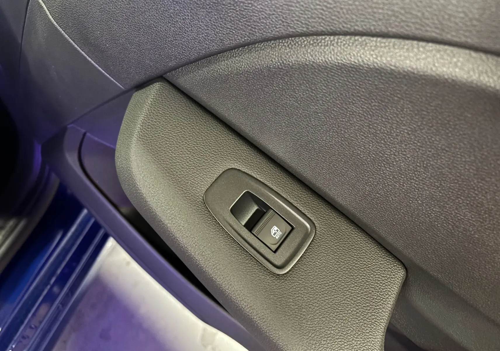 Gros plan sur la commande de lève-vitre électrique côté conducteur dans une Renault Clio bleu Iron 2024.
