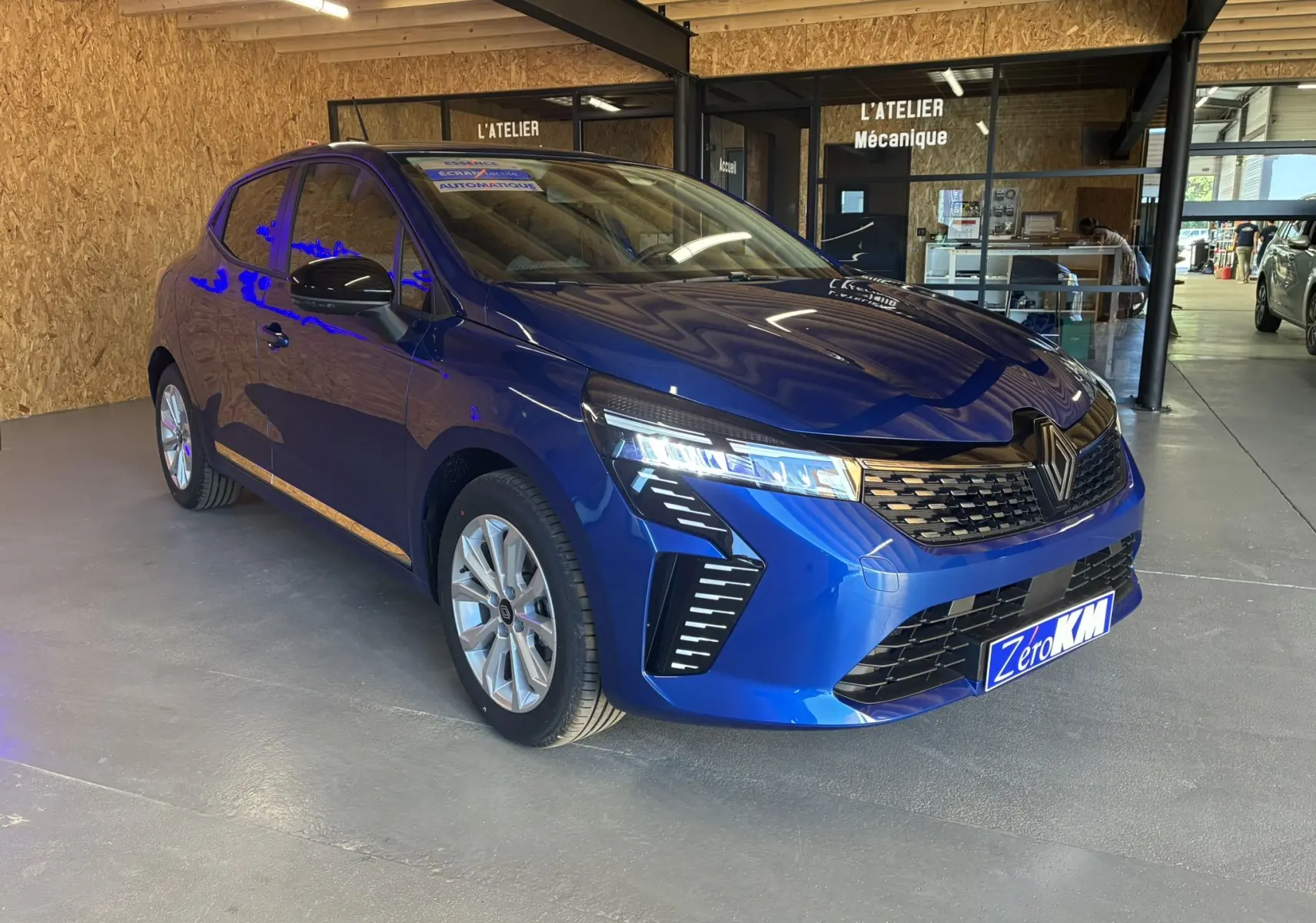 Renault Clio TCe 90ch X-Tronic Evolution bleu Iron vue 3/4 avant droit en intérieur d'atelier mécanique.