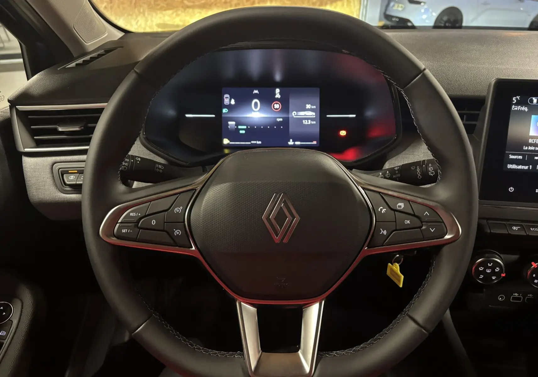 Vue intérieure centrée sur le volant de la Renault Clio 2024, avec tableau de bord numérique et commandes intégrées.
