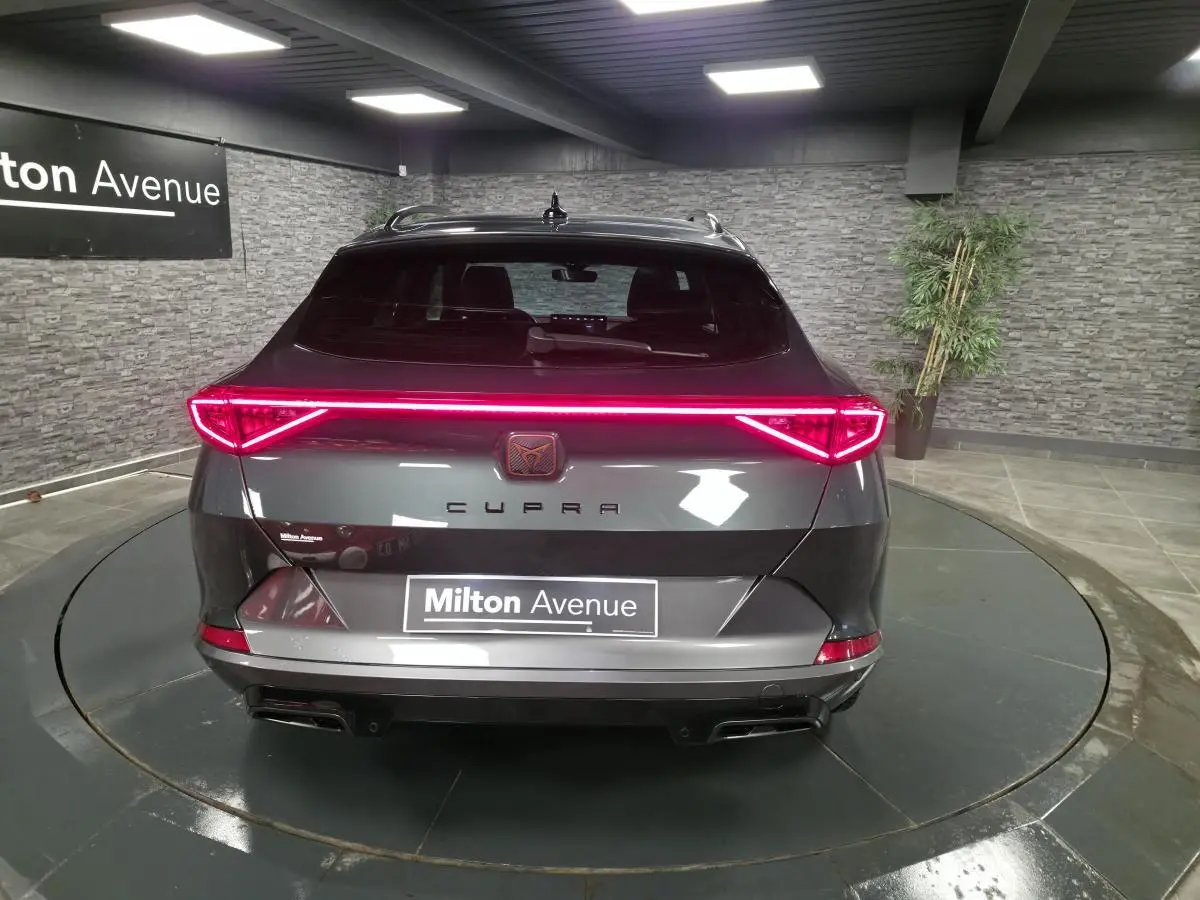 Vue arrière d'une CUPRA Formentor gris caïman avec bandeau lumineux LED et double sortie d'échappement noire dans un showroom.