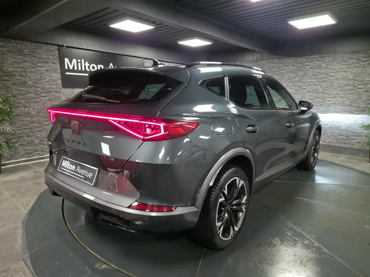 Vue 3/4 arrière droite d'une CUPRA Formentor gris caïman avec feux arrière LED en bandeau lumineux et jantes alliage 18 pouces.