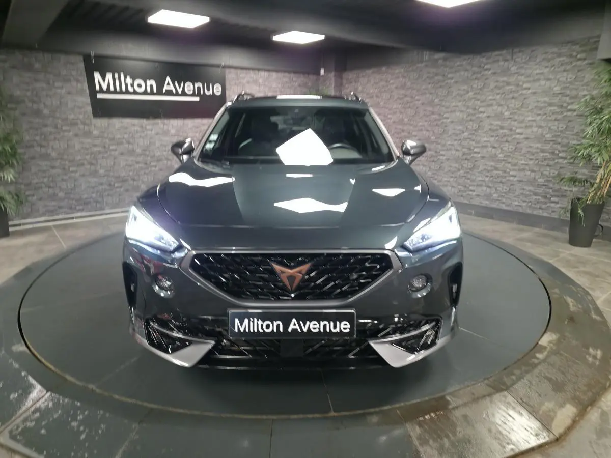 Vue de face du CUPRA Formentor gris avec calandre noire et éclairage LED allumé dans un showroom.