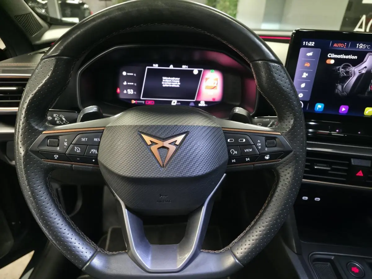 Vue rapprochée du volant sport noir perforé avec logo CUPRA cuivre et tableau de bord digital du Formentor gris.