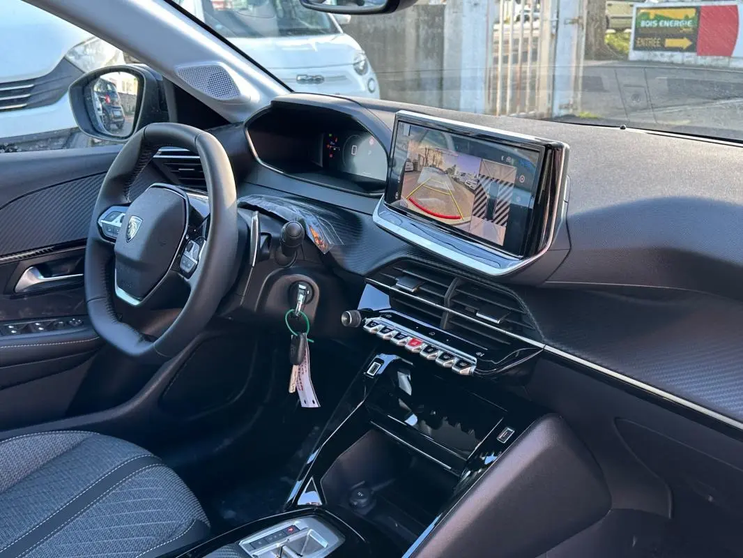 Vue intérieure côté conducteur de la Peugeot 208 Hybrid 110 Allure blanche, avec écran tactile et volant multifonction.