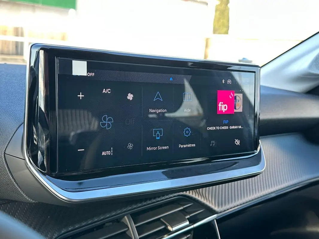 Écran tactile du tableau de bord de la Peugeot 208 Hybrid 110 blanc, vue de près côté passager.