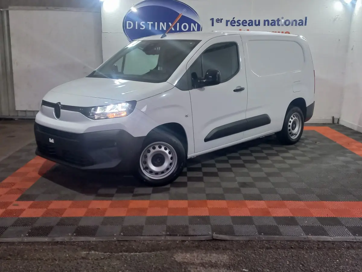 Vue 3/4 avant gauche d’un utilitaire Citroën Berlingo XL blanc avec phares allumés dans un showroom.