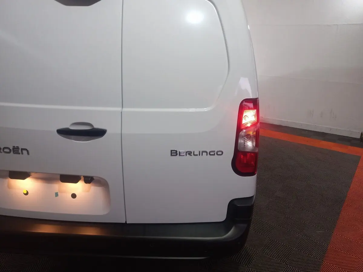 Vue arrière droite du Citroën Berlingo blanc avec feu arrière allumé dans un garage au sol noir et orange.