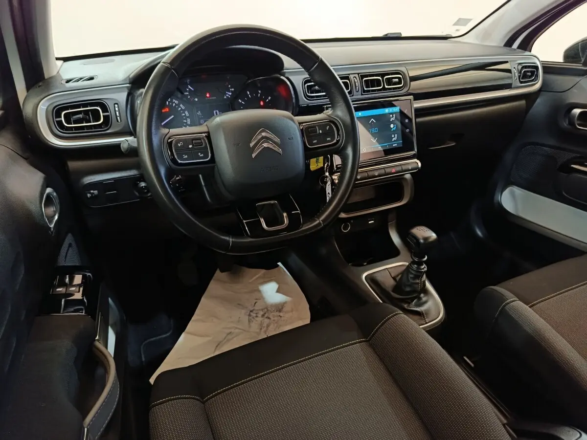 Vue intérieure côté conducteur de la Citroën C3 blanche 2021, volant cuir, écran tactile et boîte manuelle visible.