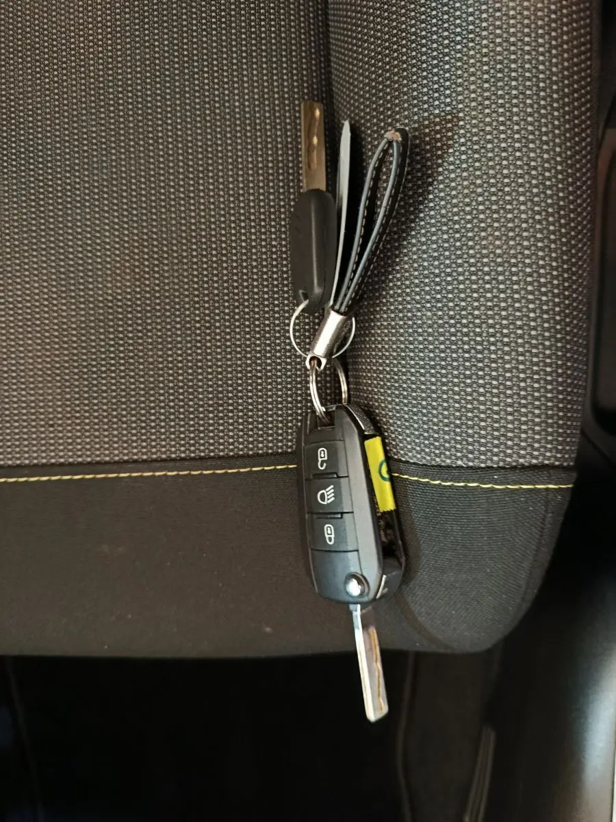 Clé de contact Citroën C3 posée sur un siège tissu gris à surpiqûres jaunes, vue rapprochée intérieure.