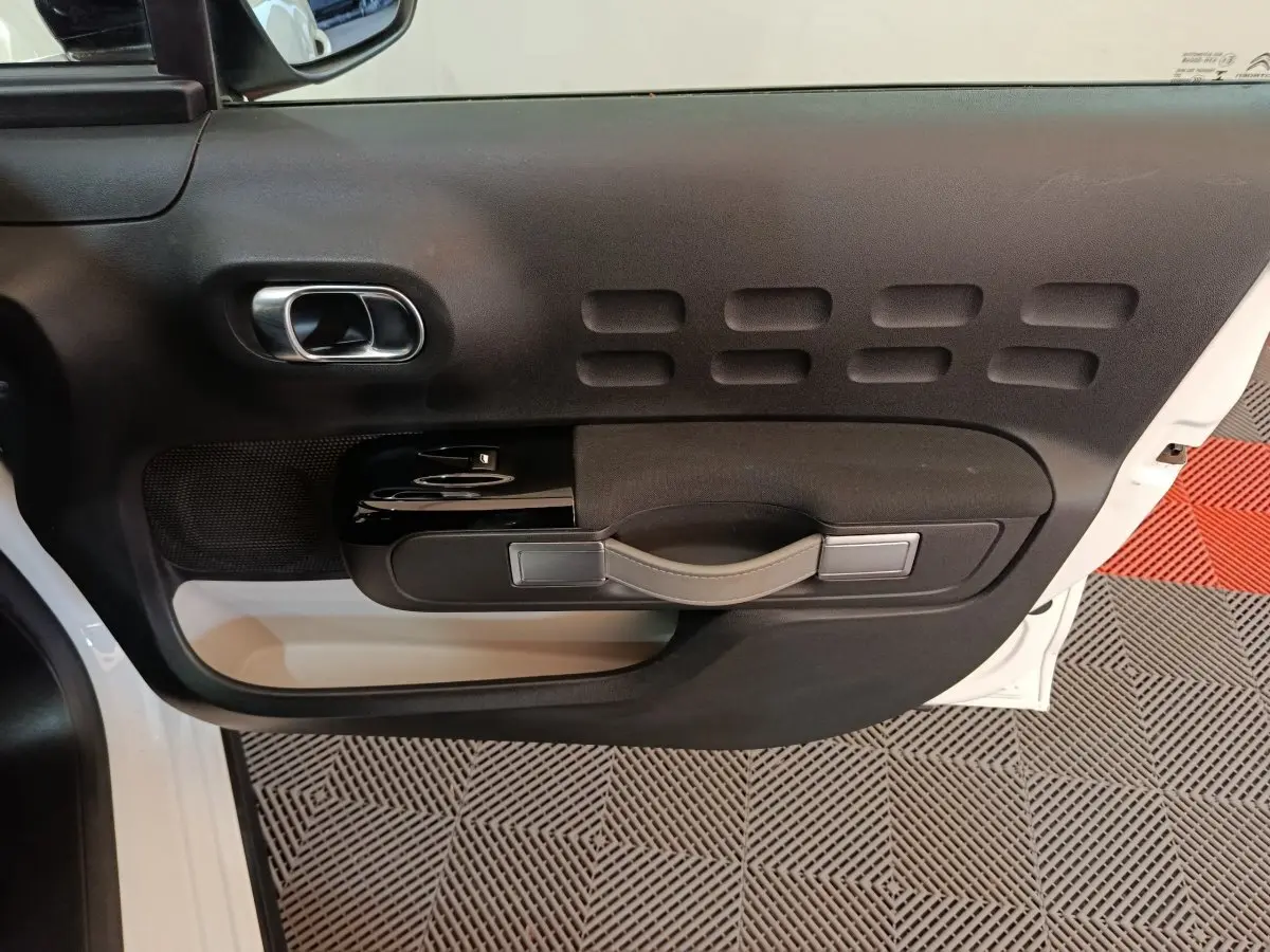 Vue rapprochée de la porte avant gauche noire et blanche de la Citroën C3 avec poignée intégrée et commandes de vitres.