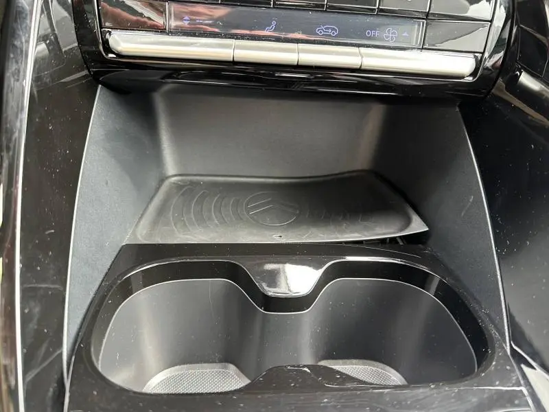 Vue rapprochée de la console centrale noire de la Citroën C3 électrique 2025 avec porte-gobelets et zone de recharge sans fil.