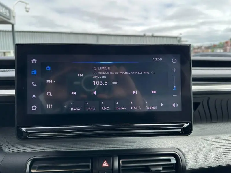 Écran tactile central de la Citroën C3 électrique 2025 affichant la radio FM, intérieur avec tableau de bord gris.