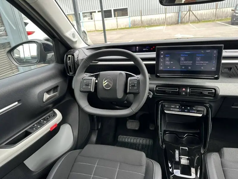 Vue intérieure de face du poste de conduite de la Citroën C3 électrique 2025 avec volant multifonction et écran tactile central.