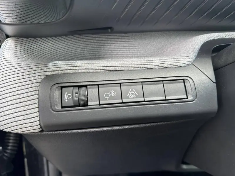 Détail des commandes de réglage d'éclairage et d'assistance sur la planche de bord côté gauche d'une Citroën C3 électrique noire.