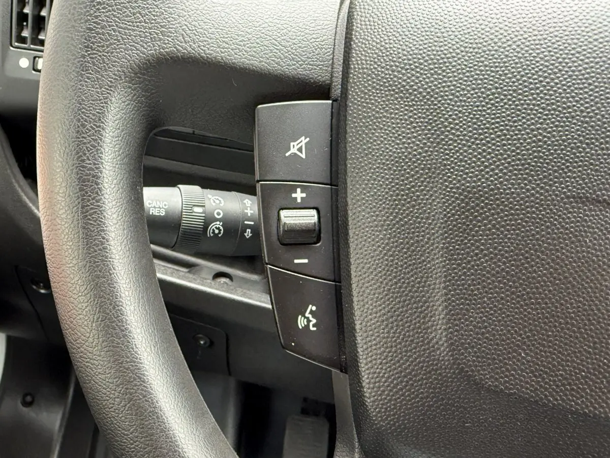 Gros plan sur le volant multifonctions noir du Peugeot Boxer Fourgon blanc, avec commandes de volume et régulateur.