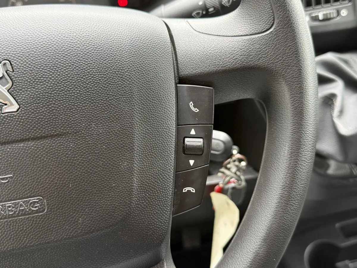 Gros plan sur le volant multifonctions noir du Peugeot Boxer Fourgon 2023 avec commandes d’appel et clé insérée.