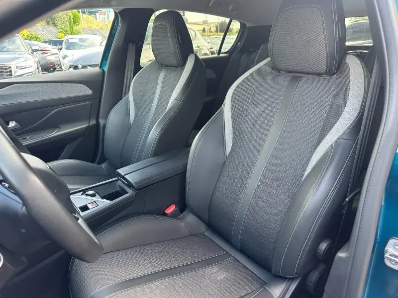 Vue intérieure côté avant droit de la Peugeot 308 2024, sièges bi-matière gris et noir avec accoudoir central.