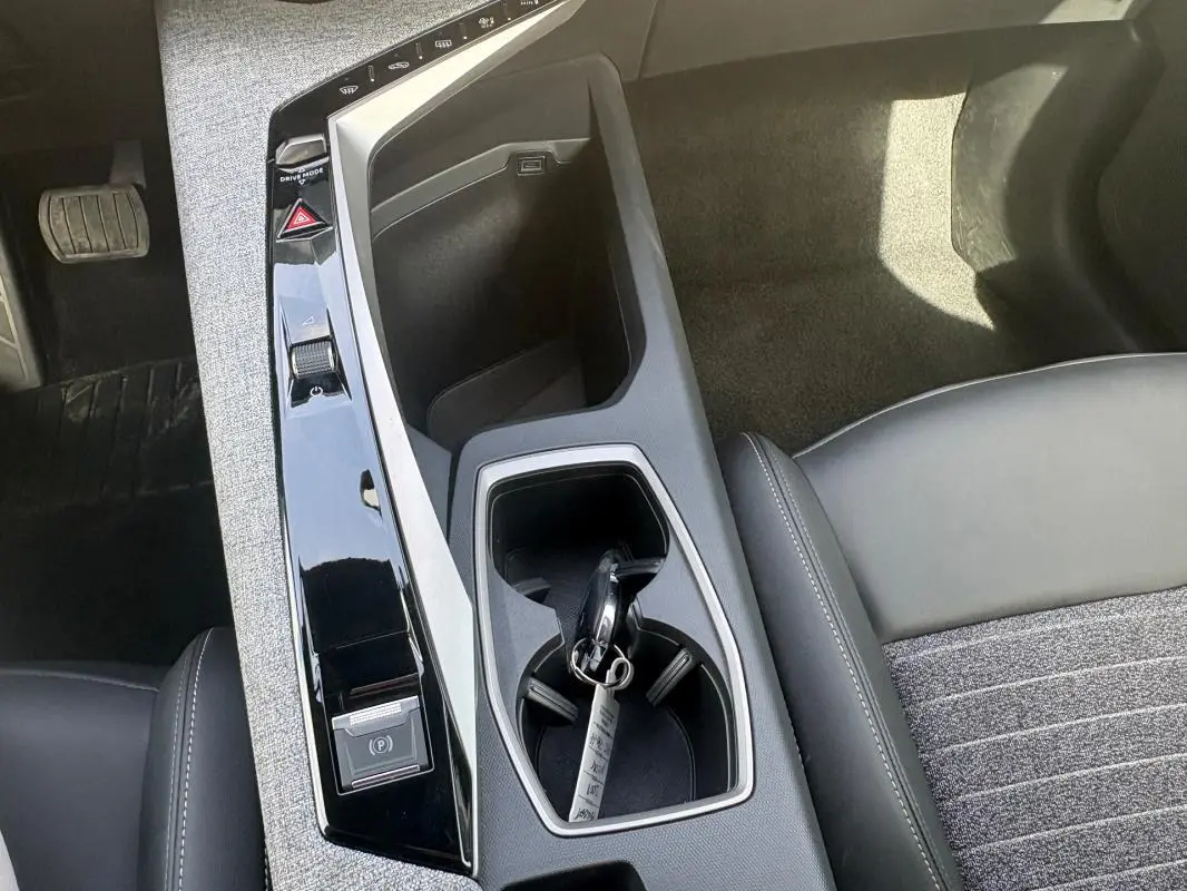Vue plongeante sur la console centrale noire du Peugeot 3008 Hybrid 136 e-DCS6 Allure avec clé dans porte-gobelet.