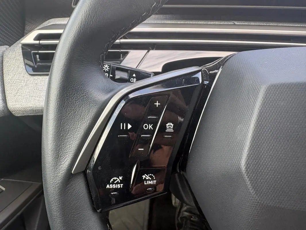 Gros plan sur les commandes au volant à gauche du Peugeot 3008 Hybrid noir, avec boutons de régulateur et assistance.