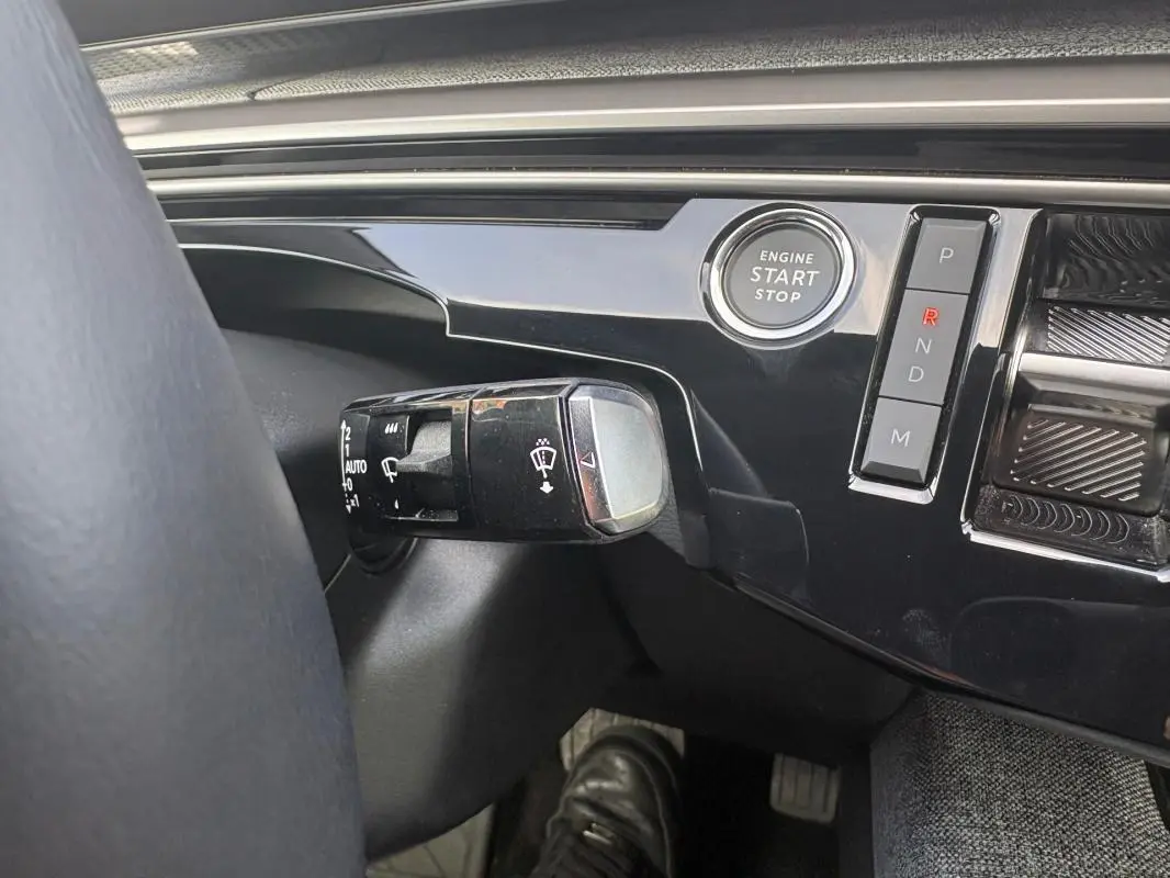 Gros plan sur la commande d’essuie-glace et le bouton start/stop du tableau de bord noir du Peugeot 3008 Hybrid 2025.
