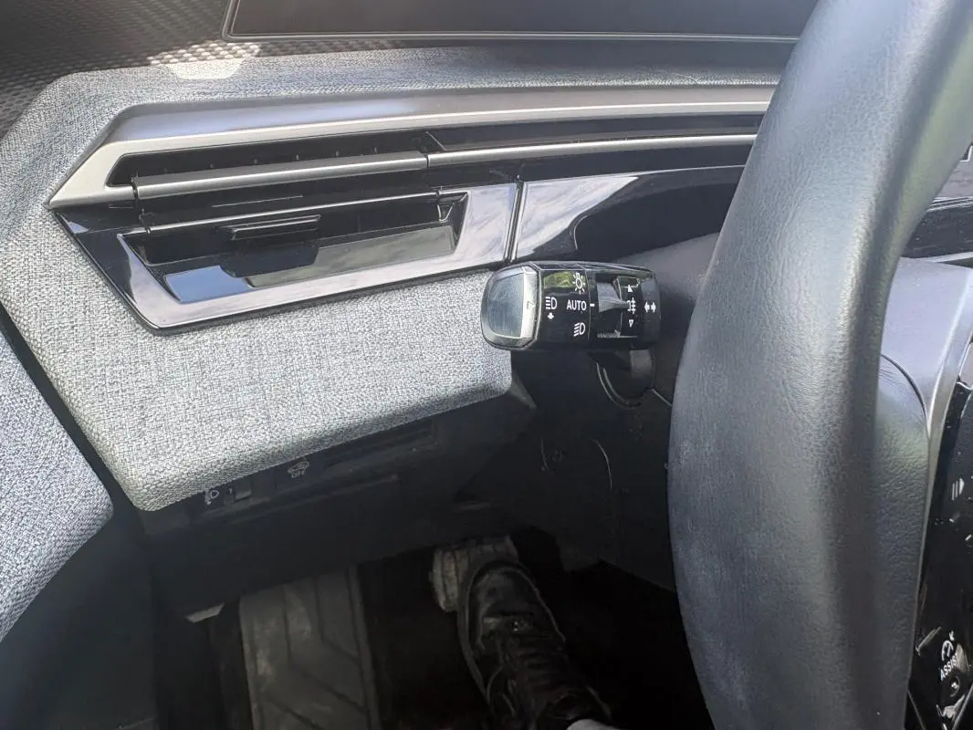 Détail intérieur côté gauche du Peugeot 3008 Hybrid 2025, montrant la commande d’allumage automatique des feux et la finition tissu grise.