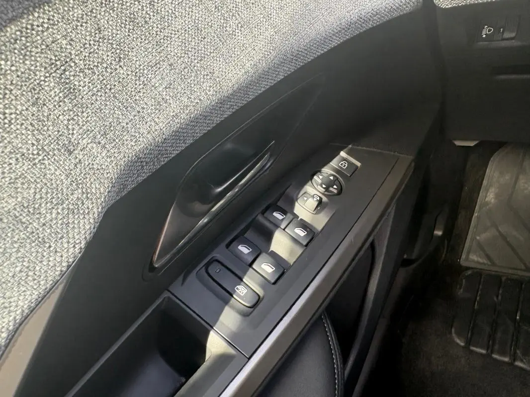 Gros plan sur la commande des vitres côté gauche de la Peugeot 3008 Hybrid noire, avec habillage tissu gris et plastique noir.