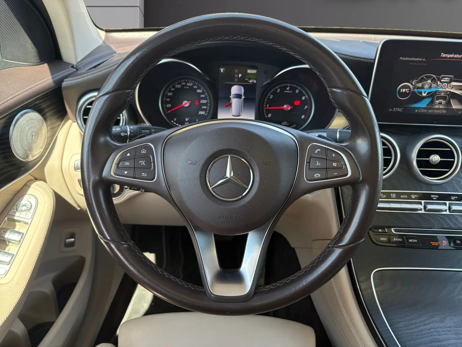 Vue intérieure centrée sur le volant cuir marron et tableau de bord beige du Mercedes GLC 350 E HYBRID FASCINATION 2017.