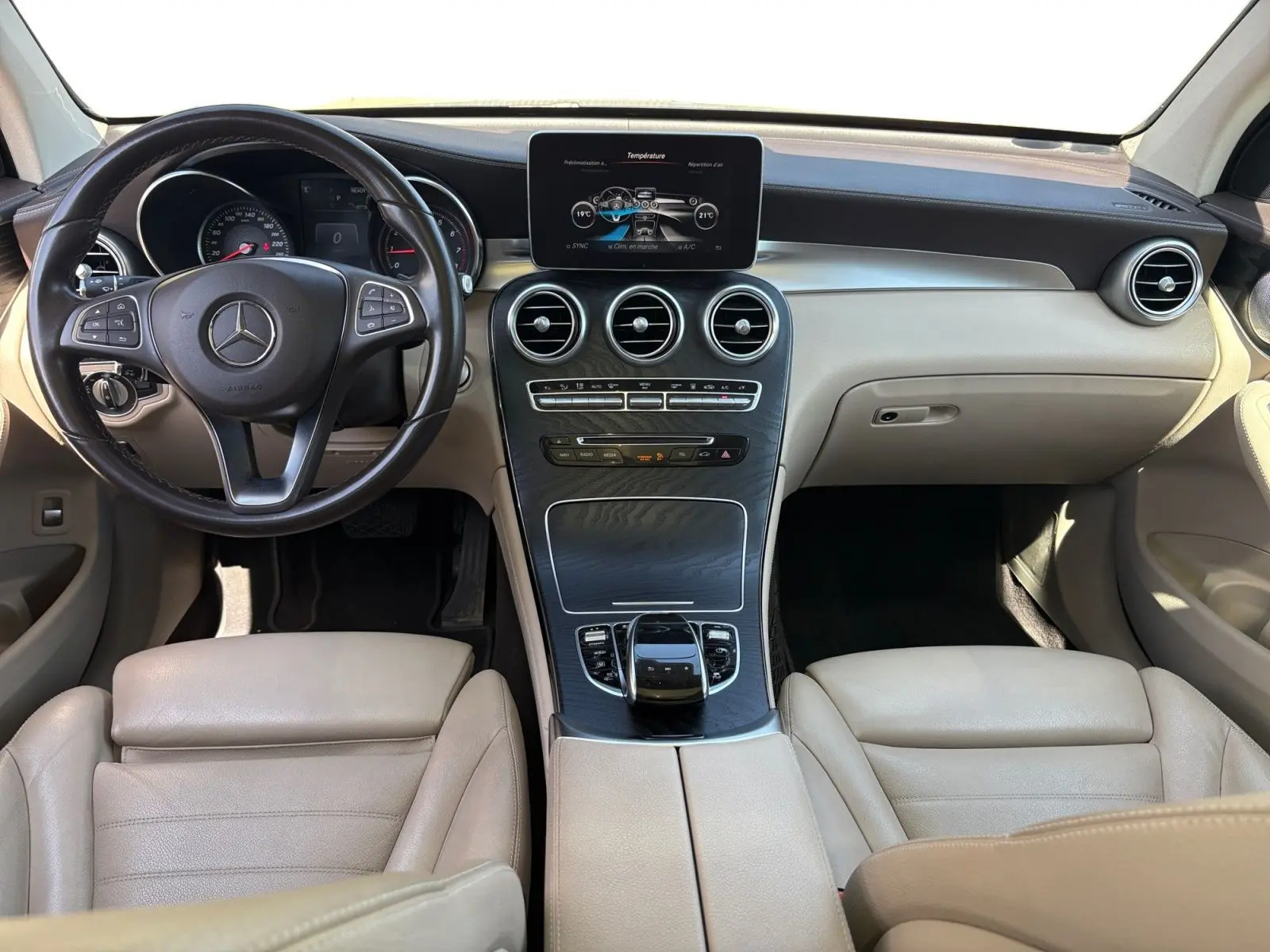 Vue intérieure frontale du tableau de bord beige et noir du Mercedes GLC 350 E Hybrid Fascination avec écran central et volant cuir.